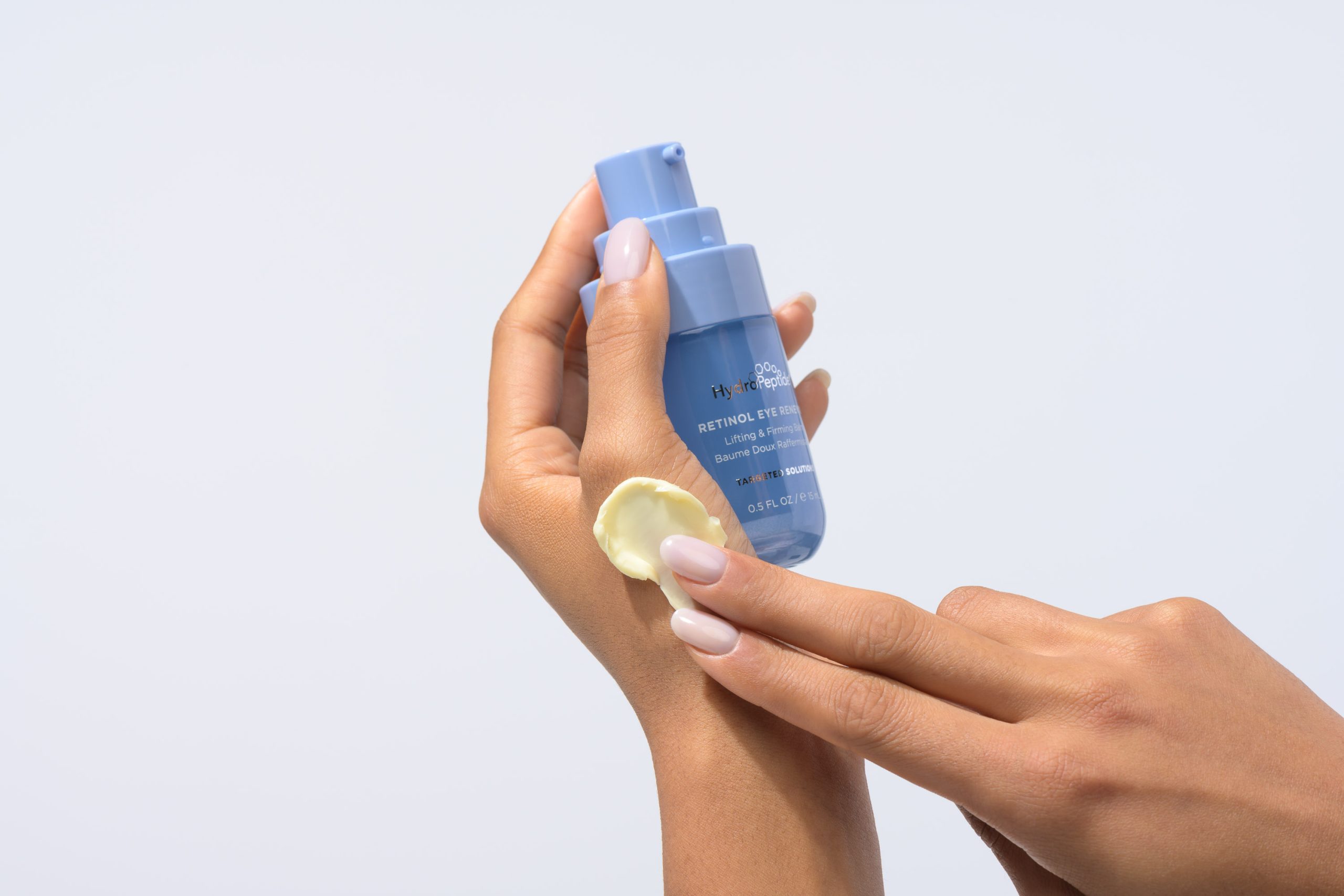 Hands applying HydroPeptide Retinol Eye Renewal balm to the back of a hand.