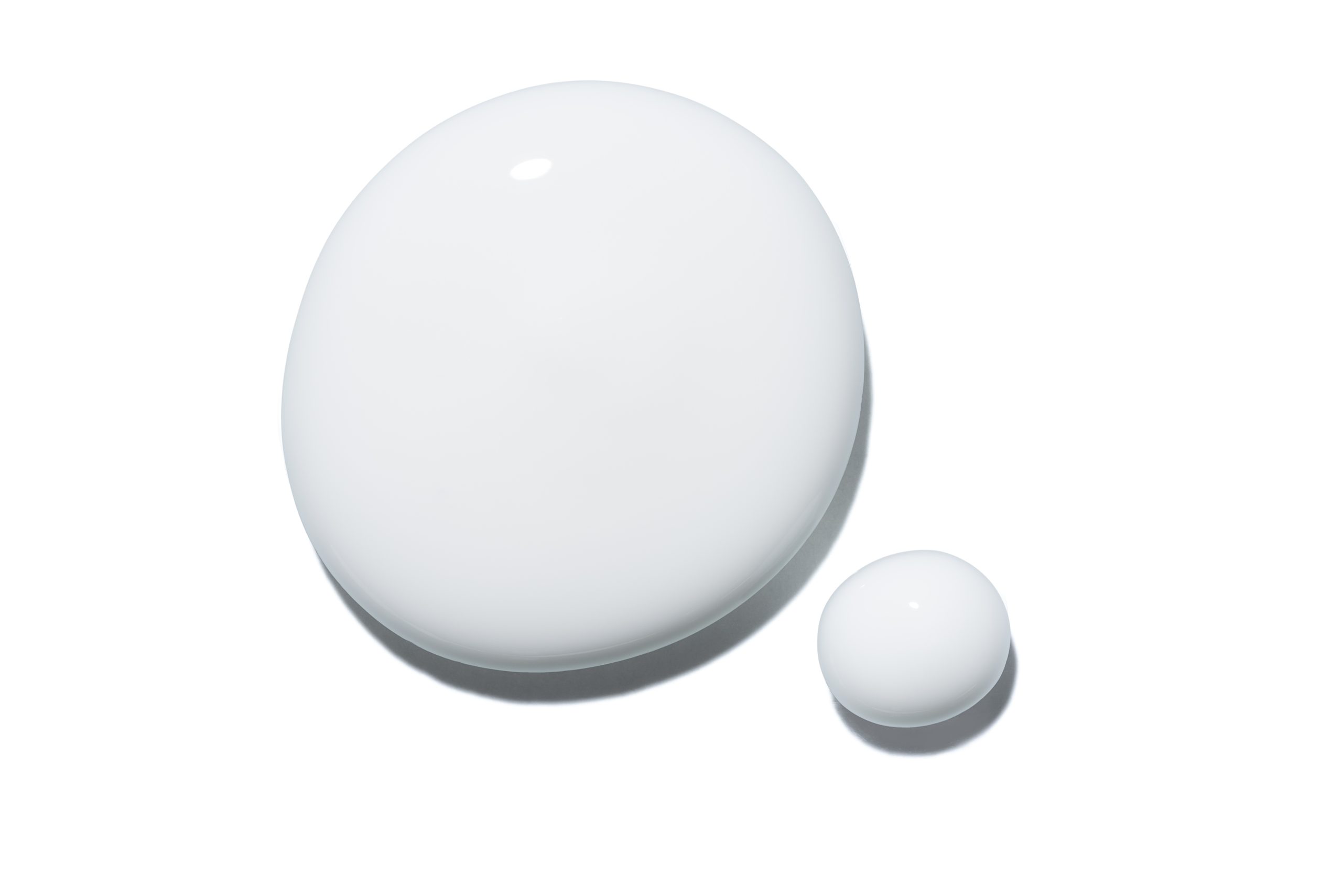 Based on the image "image_4b4584.jpg", it shows two drops of an opaque white liquid, one large and one small, resting on a white background.
