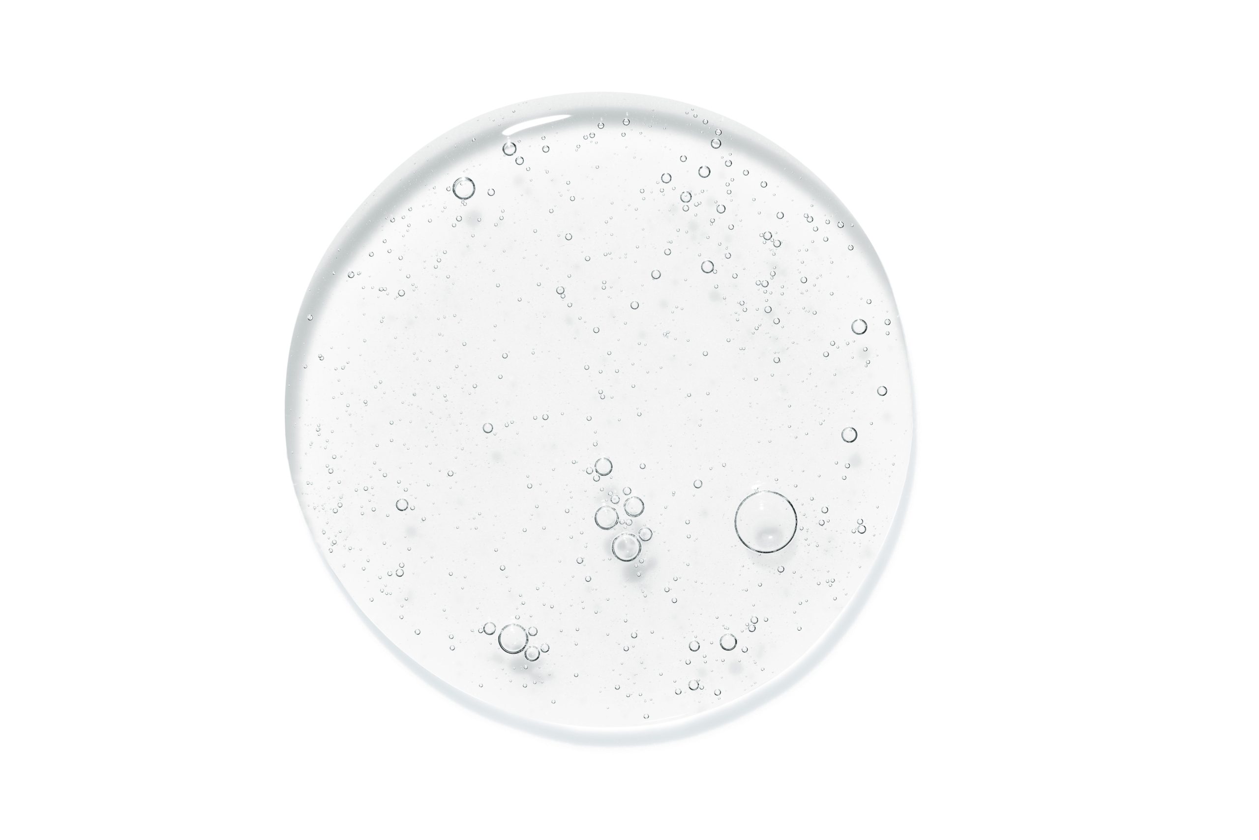 Clear liquid drop with bubbles on white surface.